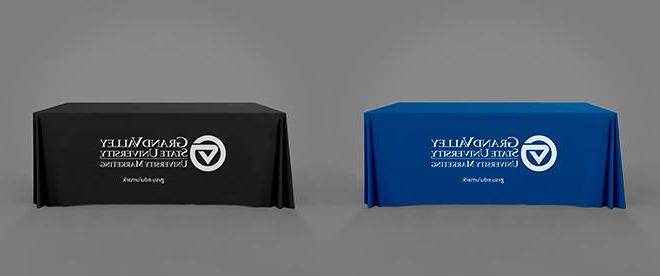 A table with a blue throw on it adjacent to a table with a black throw on it. Both throws have a white Grand Valley 大学市场营销 logo on them.